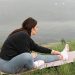 A woman stretches on a yoga mat by a serene lake, embodying relaxation and wellness in nature.